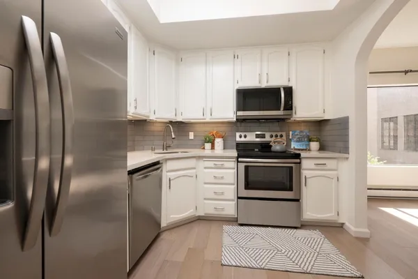 a kitchen with stainless steel appliances granite countertop a refrigerator a stove a sink and a white cabinets