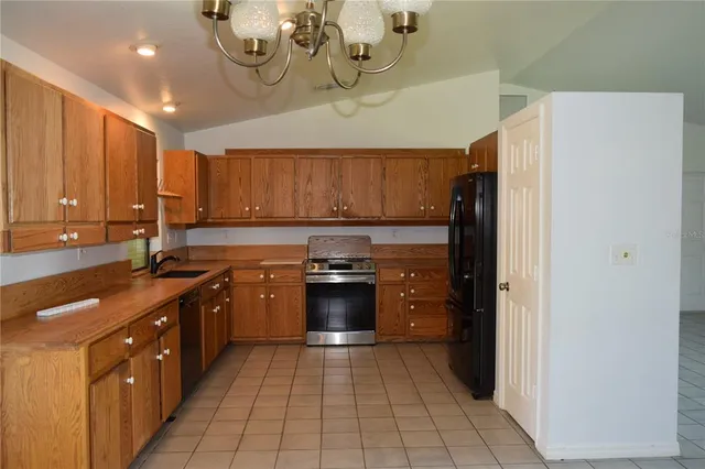 a kitchen with stainless steel appliances granite countertop a refrigerator a sink dishwasher a stove and a dining table with wooden cabinet