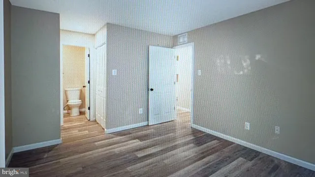 a view of an empty room with wooden floor and a bathroom