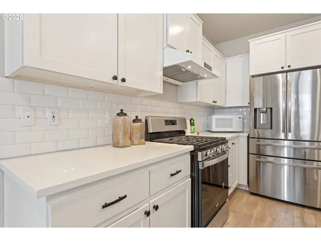 a kitchen with stainless steel appliances a stove a refrigerator a sink and white cabinets