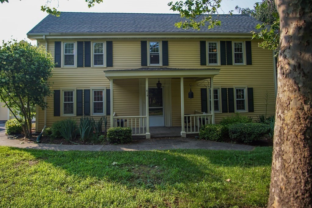 a view of a brick house with a yard potted plants and a large tree