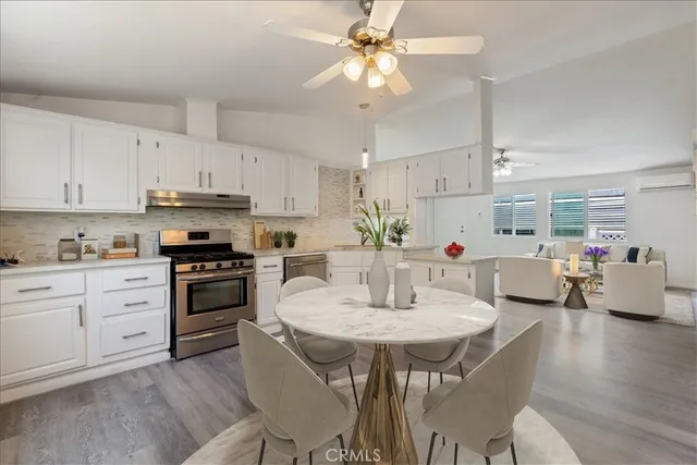 a kitchen with stainless steel appliances kitchen island granite countertop a table chairs stove and white cabinets
