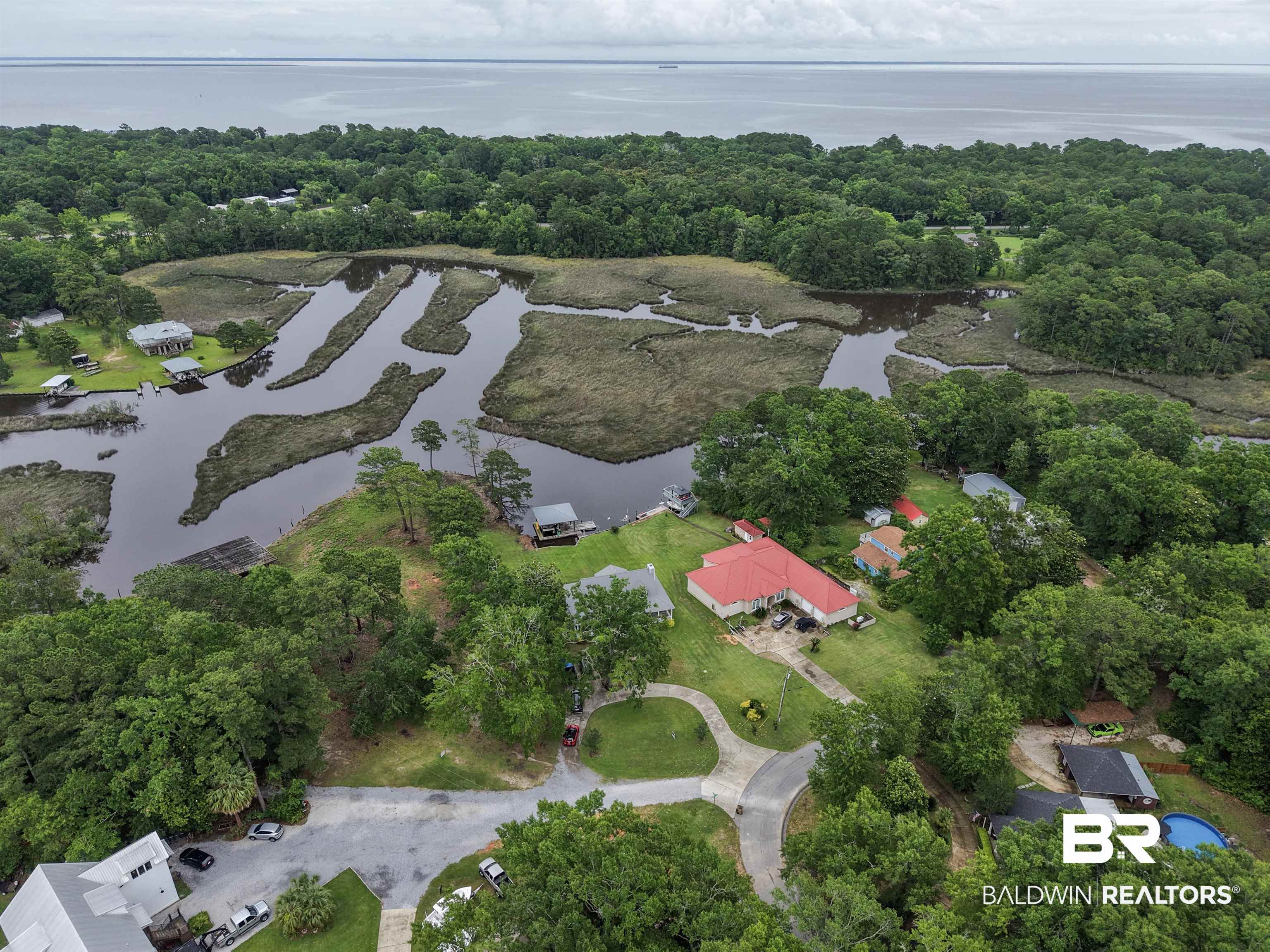 12171 Marguerite Drive Coden, AL 36523 - Photo 26 of 44 Expansive waterfront property featuring a red metal roof structure, circular driveway, and established trees
