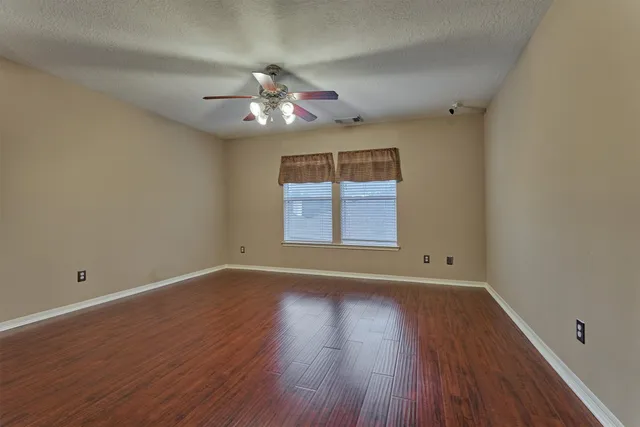 an empty room with wooden floor chandelier fan and windows