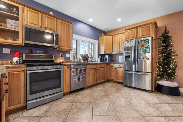 a kitchen with stainless steel appliances granite countertop a stove a refrigerator a sink a dining table and chairs with wooden floor