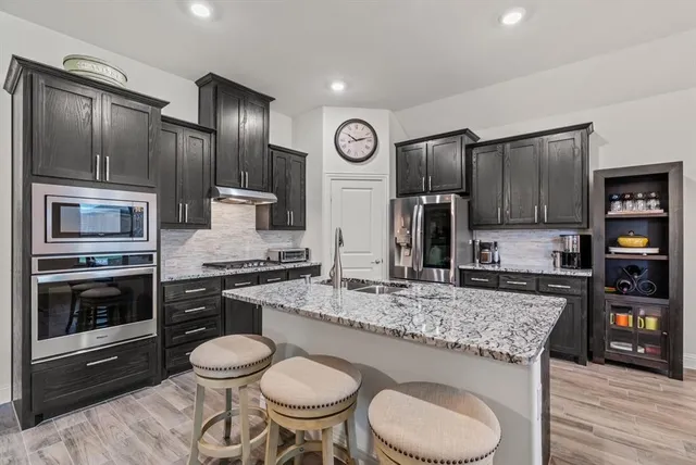 a kitchen with stainless steel appliances granite countertop a stove a sink dishwasher a refrigerator and wooden cabinets with wooden floor