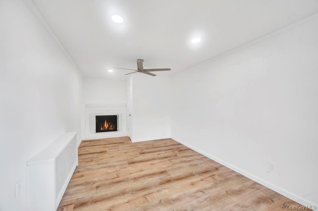 815 Udall Road West Islip, NY 11795 - Photo 18 of 45 Unfurnished living room featuring light wood-style floors, a fireplace, radiator heating unit, ceiling fan, and crown molding