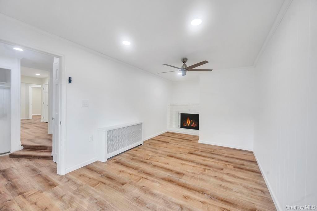 815 Udall Road West Islip, NY 11795 - Photo 19 of 45 Unfurnished living room featuring radiator heating unit, a lit fireplace, light wood-type flooring, ceiling fan, and recessed lighting