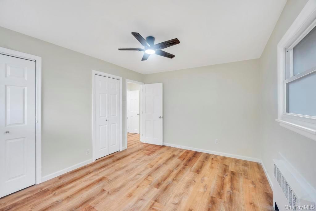 815 Udall Road West Islip, NY 11795 - Photo 36 of 45 Unfurnished bedroom featuring radiator heating unit, light wood-style floors, multiple closets, and ceiling fan