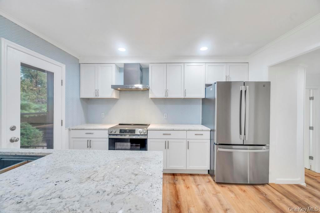 815 Udall Road West Islip, NY 11795 - Photo 6 of 45 Kitchen featuring appliances with stainless steel finishes, ornamental molding, wall chimney exhaust hood, light wood-type flooring, and white cabinetry