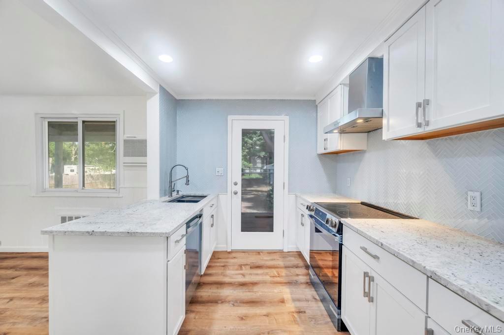 815 Udall Road West Islip, NY 11795 - Photo 8 of 45 Kitchen with backsplash, black range with electric stovetop, a peninsula, wall chimney range hood, and white cabinetry