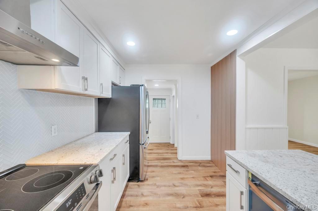 815 Udall Road West Islip, NY 11795 - Photo 9 of 45 Kitchen featuring white cabinets, light stone countertops, appliances with stainless steel finishes, wall chimney exhaust hood, and light wood-style flooring