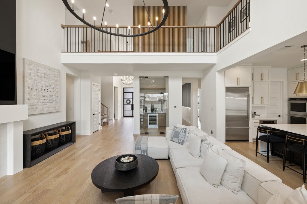 802 Geiger Path Austin, TX 78738 - Photo 34 of 40 View towards the upstairs landing and front entry of the home. The open-concept living area, showcasing soaring ceilings, suspended lighting, light wood floors, a sleek kitchen with island seating, and a glass-enclosed wet bar with wine cooler.