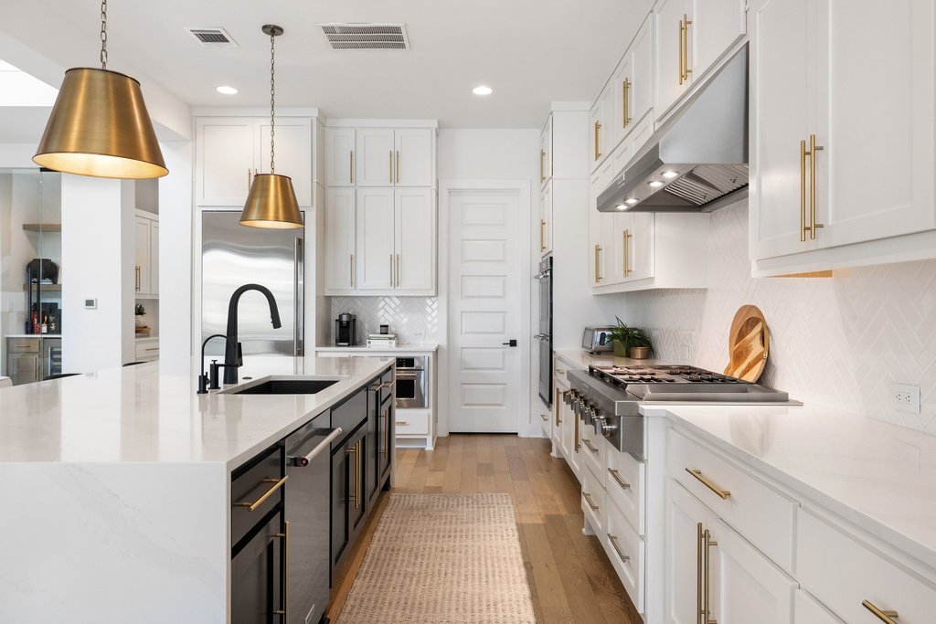 802 Geiger Path Austin, TX 78738 - Photo 4 of 40 Gourmet kitchen with sleek countertops, two-tone cabinetry, professional-grade stainless steel appliances, and a large island with black matte faucet and pendant lighting.
