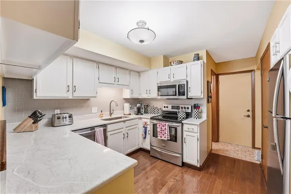 a kitchen with stainless steel appliances granite countertop a stove top oven a sink a refrigerator and white cabinets with wooden floor