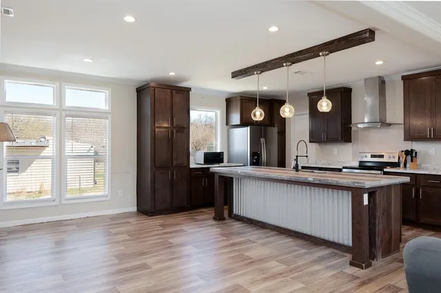 a large kitchen with stainless steel appliances granite countertop a refrigerator a sink dishwasher a stove and a dining table with wooden floor
