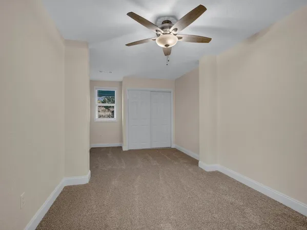 an empty room with a chandelier fan and windows