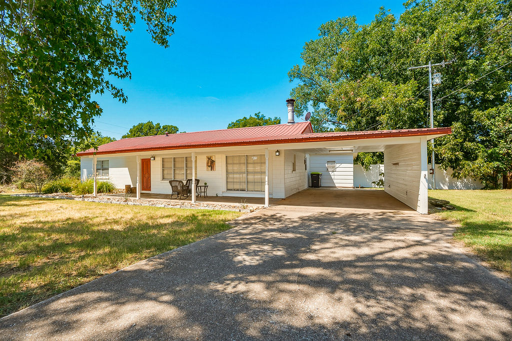 1009 Southeast County Road Ada, OK 74820 - Photo 84 of 92 White exterior with a red metal roof, covered carport, and covered front porch with stone foundation accents