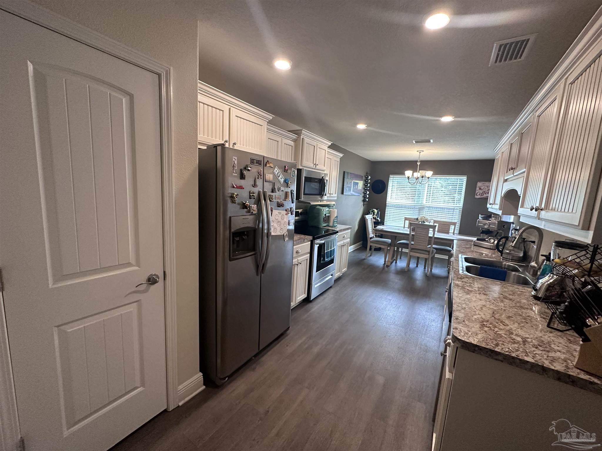 5217 Saufley Field Road Pensacola, FL 32526 - Photo 12 of 26 a kitchen with stainless steel appliances granite countertop a refrigerator a sink dishwasher a stove and a dining table with wooden floor