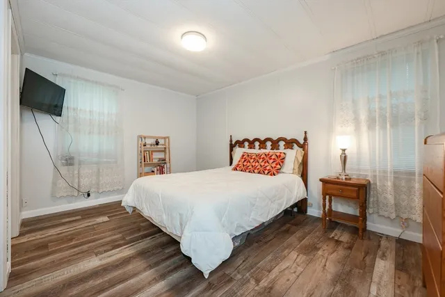 a bedroom with a bed a mirror on dresser and a wooden floor