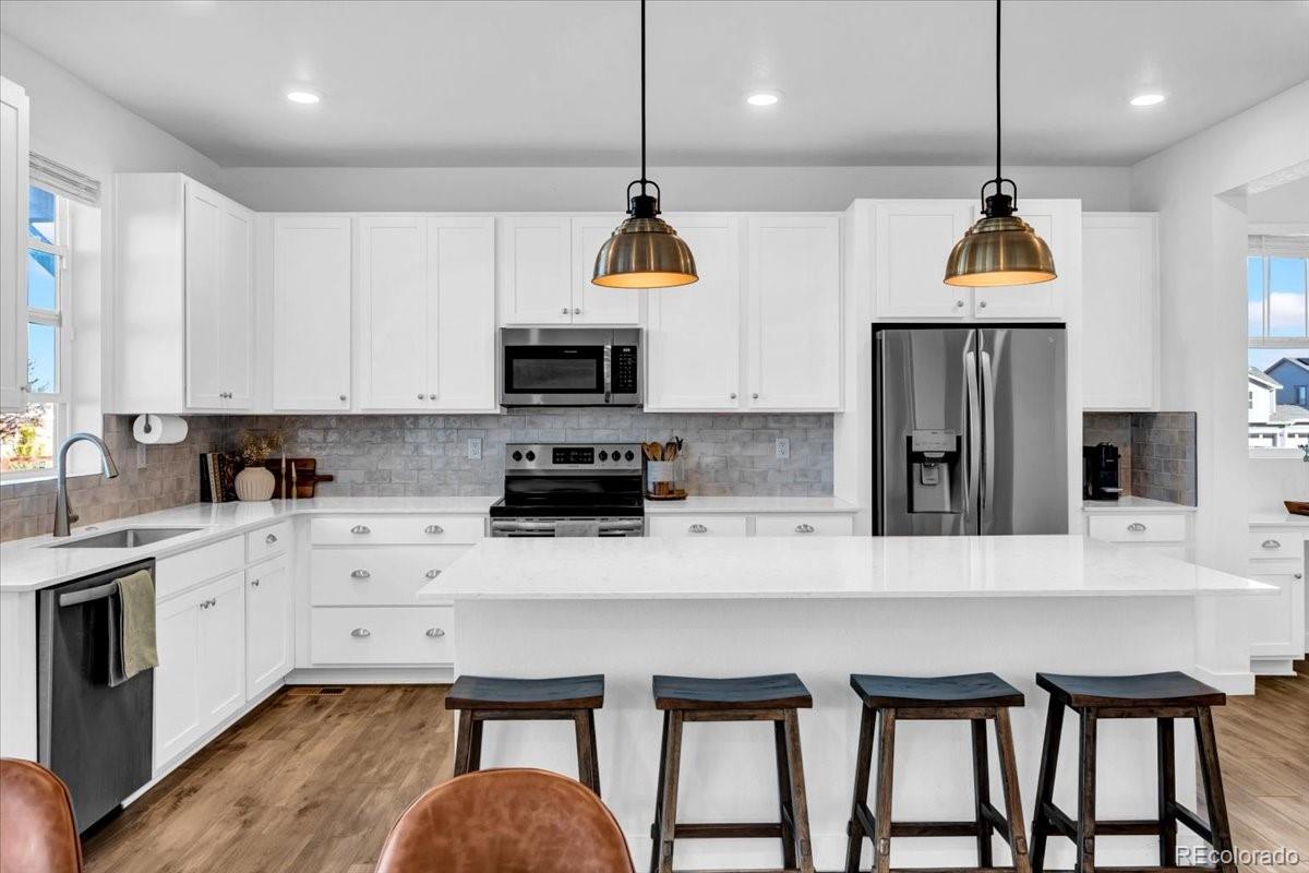 5453 Inland Avenue Firestone, CO 80504 - Photo 16 of 49 a kitchen with kitchen island granite countertop a stove a refrigerator a oven a sink a dining table and chairs with wooden floor