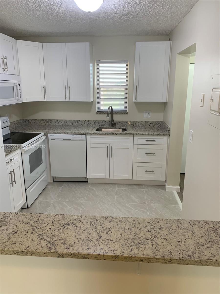 9273 Southwest 8th Street, Unit 411 Boca Raton, FL 33428 - Photo 4 of 21 a kitchen with granite countertop a sink a stove and cabinets