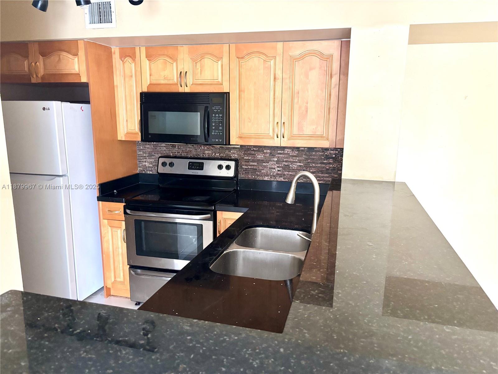 777 Southwest 111th Way, Unit 101 Pembroke Pines, FL 33025 - Photo 5 of 7 a kitchen with granite countertop a refrigerator and a stove