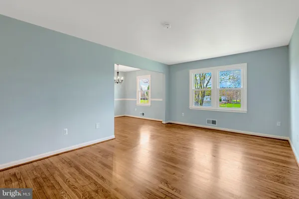 an empty room with wooden floor chandelier and windows