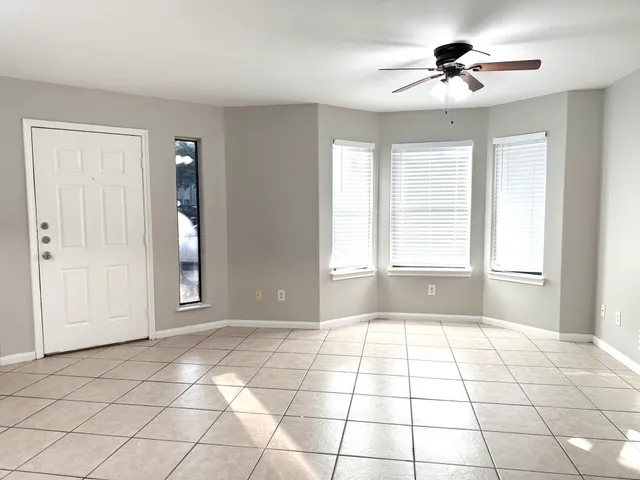 a view of an empty room with window and chandelier fan