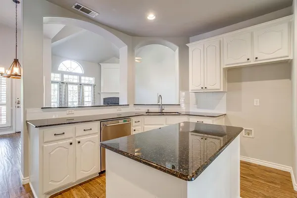a kitchen with granite countertop a sink dishwasher and white cabinets with wooden floor