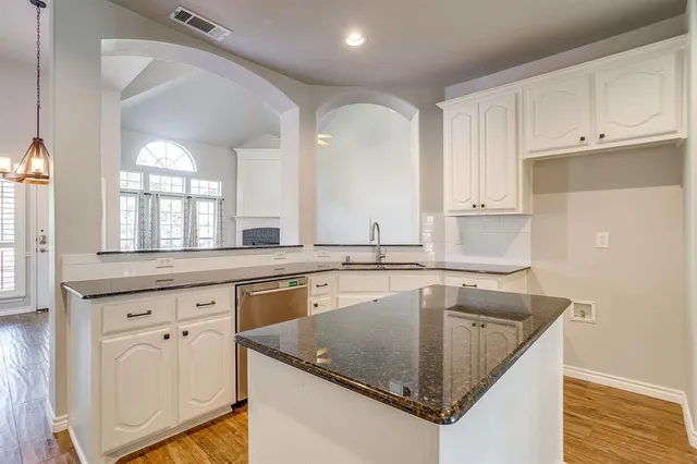 a kitchen with granite countertop a sink dishwasher and white cabinets with wooden floor