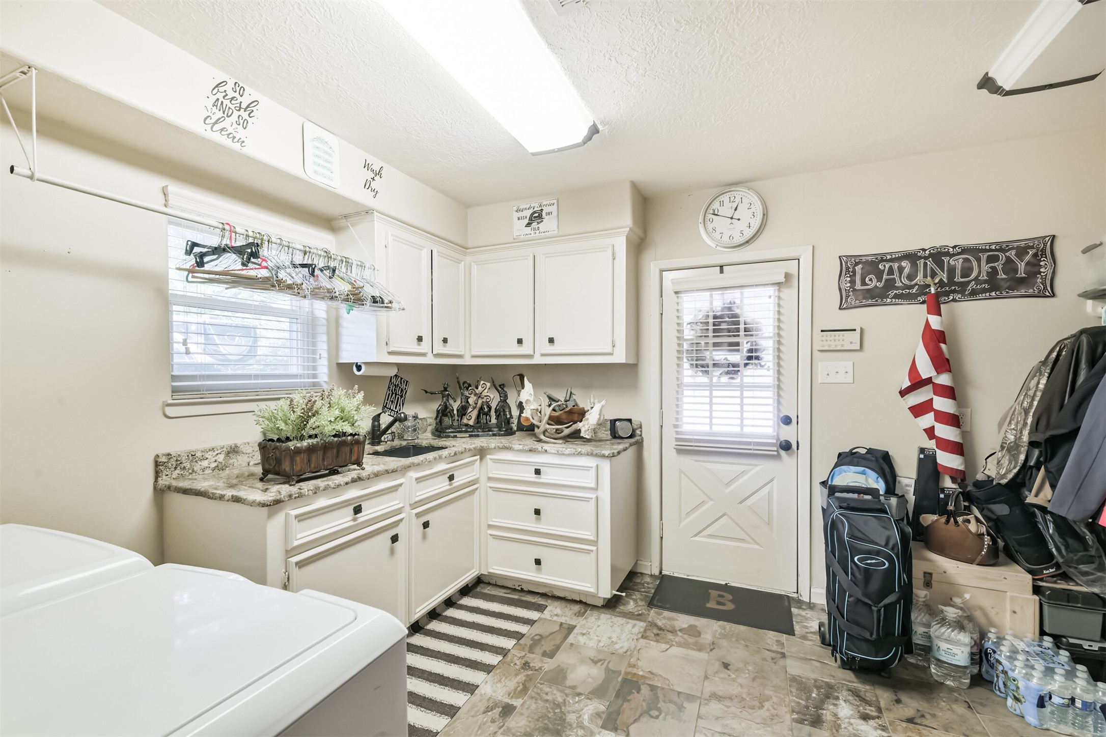 307 West Hufsmith Road Tomball, TX 77375 - Photo 21 of 44 Charming laundry room with ample cabinetry, marble countertops, and a convenient drying rack. The space is brightened by a window and has easy access to the outdoors through a back door, creating a functional and inviting area.