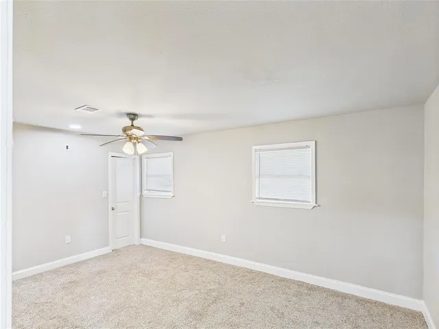 an empty room with chandelier fan and windows