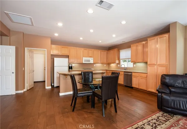 a kitchen with stainless steel appliances kitchen island granite countertop a refrigerator a stove a sink a dining table and chairs with wooden floor