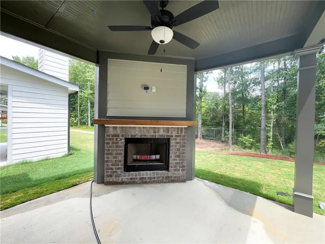a view of an empty room with a fireplace a ceiling fan and windows