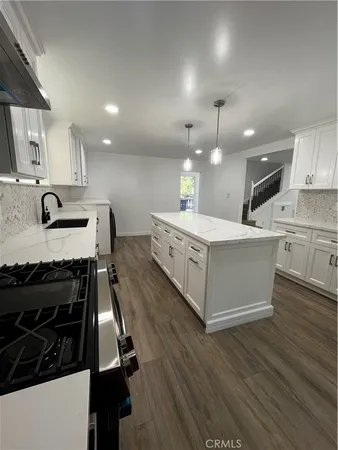 a large white kitchen with kitchen island a sink wooden floor and a refrigerator