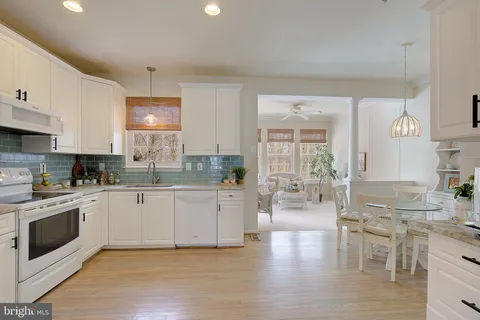 a large kitchen with stainless steel appliances a stove a sink dishwasher a microwave oven with white cabinets and wooden floor