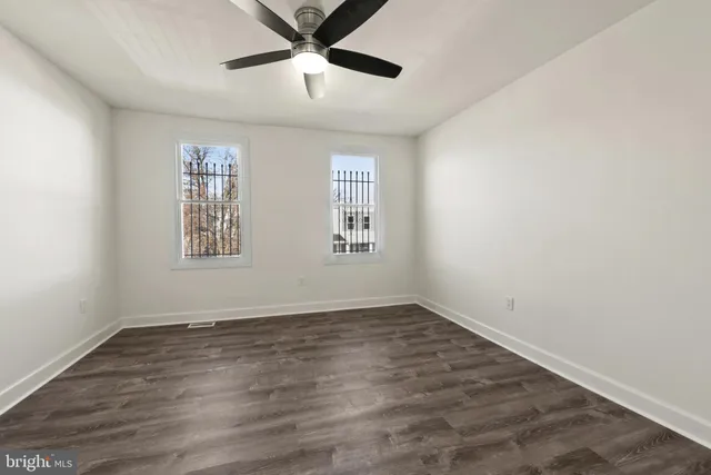 an empty room with wooden floor ceiling fan and windows