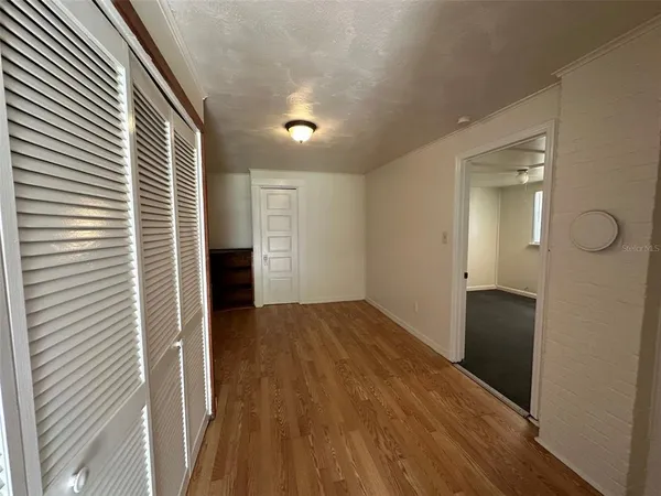a view of a hallway to an empty room with wooden floor and a window