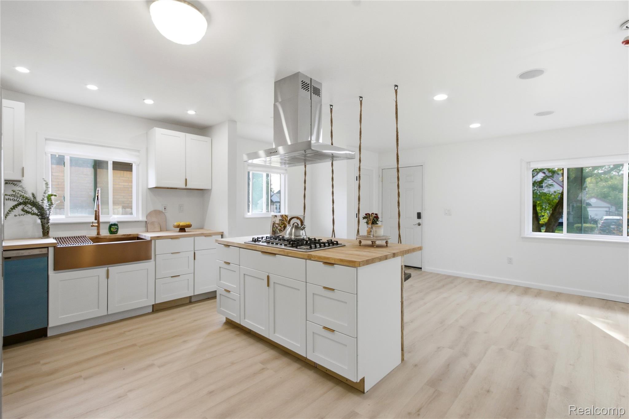 Modern kitchen featuring white cabinetry, light wood-finish countertops, light wood-finish flooring, a copper-toned farmhouse sink, and a stainless steel range hood