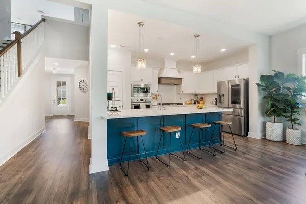 a kitchen with stainless steel appliances kitchen island granite countertop a sink a stove a refrigerator and white cabinets with wooden floor