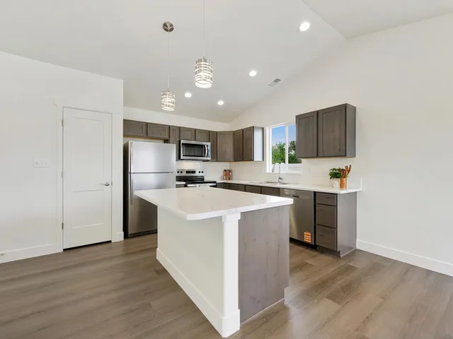 a view of kitchen with stainless steel appliances granite countertop a stove top oven a refrigerator a sink and a oven with wooden floor