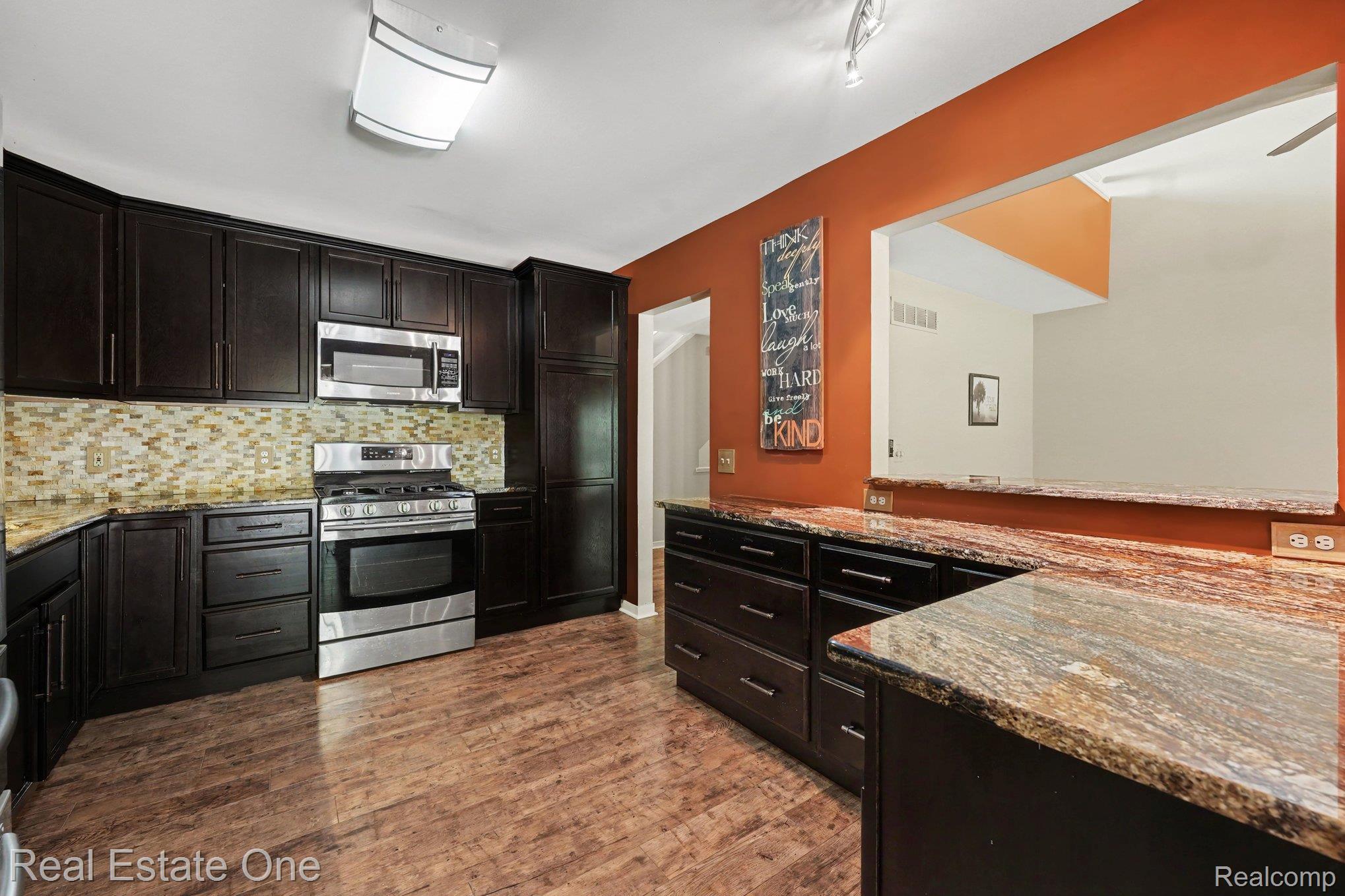701 Charing Court Rochester, MI 48307 - Photo 8 of 29 Kitchen featuring dark wood cabinetry, stainless steel appliances, a mosaic tile backsplash, and stone countertops