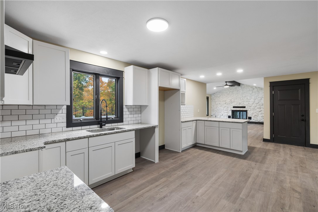 2201 Ridgewood Road Medina, OH 44256 - Photo 15 of 50 Kitchen with a peninsula, light wood-type flooring, a fireplace, under cabinet range hood, and white cabinetry