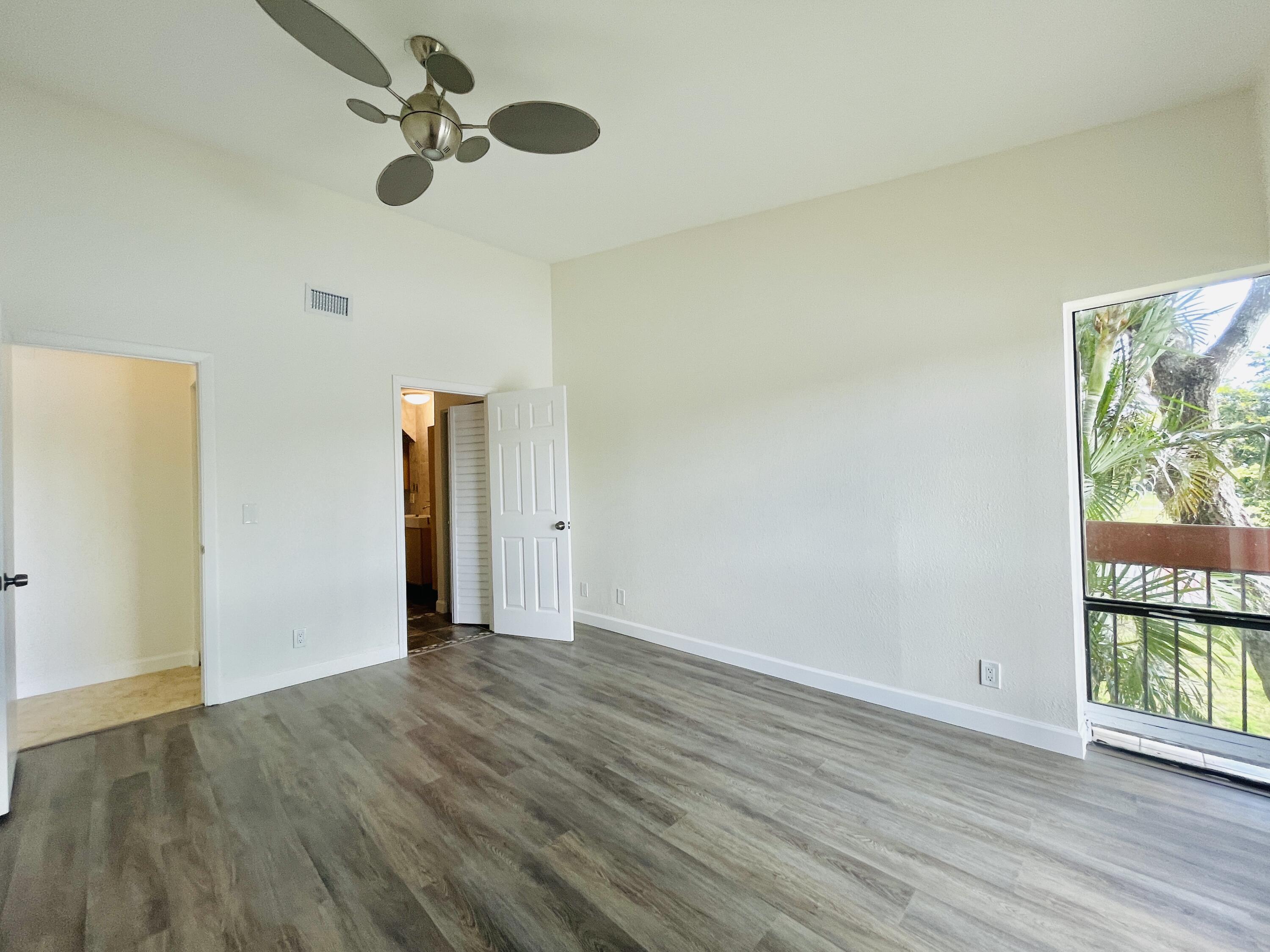 2297 Southwest 15th Street, Unit 122 Deerfield Beach, FL 33442 - Photo 13 of 47 an empty room with wooden floor chandelier fan and windows