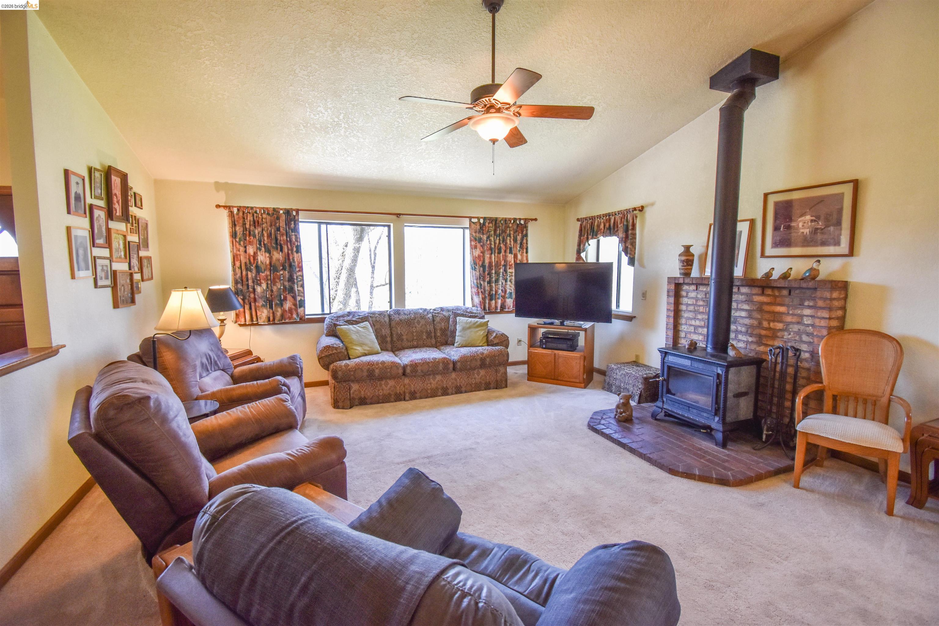 15170 Potato Ranch Road Sonora, CA 95370 - Photo 9 of 49 Living room with a wood stove, light colored carpet, ceiling fan, and plenty of natural light