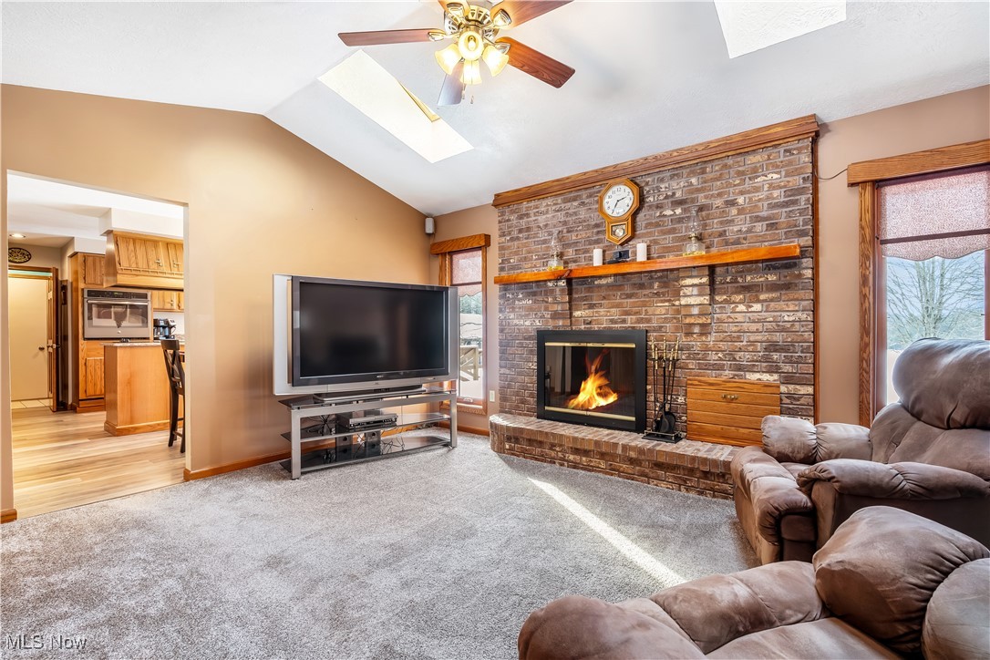 1037 Atkins Road Geneva, OH 44041 - Photo 6 of 50 Inviting living room showcases a striking curved brick wood-burning fireplace with cherry mantel and exterior-access wood storage, complemented by a beautiful arched pass-through window and skylights that flood the space with natural light.