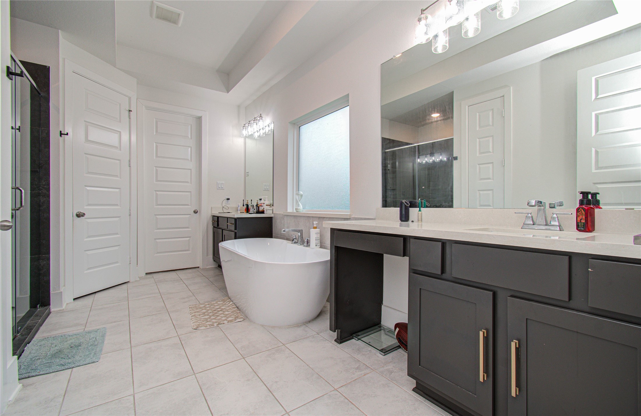 4211 Limestone Terrace Manvel, TX 77578 - Photo 18 of 33 This bathroom features a modern design with a freestanding tub, spacious vanity with dual sinks, large mirrors, and a glass-enclosed shower. It offers ample natural light, complemented by sleek cabinetry and stylish fixtures.