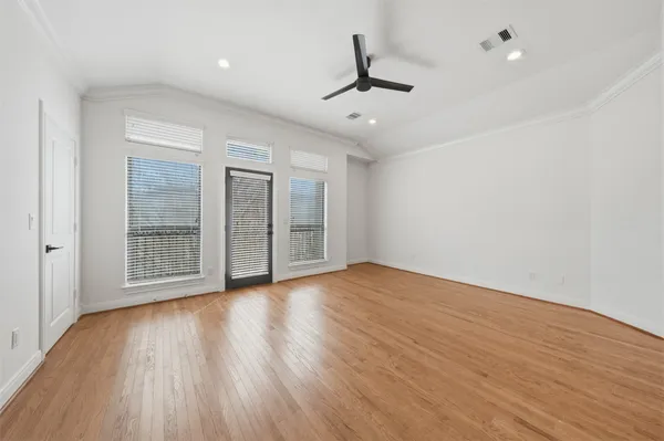 a view of an empty room with wooden floor and a ceiling fan