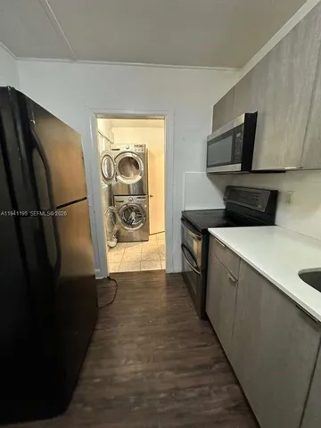a view of a refrigerator in kitchen and an empty room with wooden floor windows